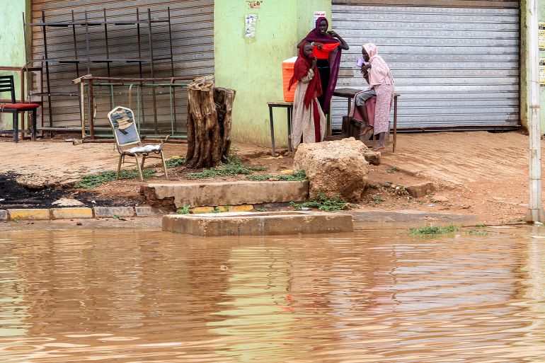 TOPSHOT - Women gather along the side of a flooded street in Sudan's capital Khartoum following heavy rain on آب 27, 2025. (Photo by Ebrahim Hamid / AFP)