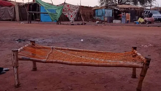صورة تُظهر سريراً مصنوعاً من الخيوط وأغصان الأشجار موضوعاً فوق طريق موحل.
