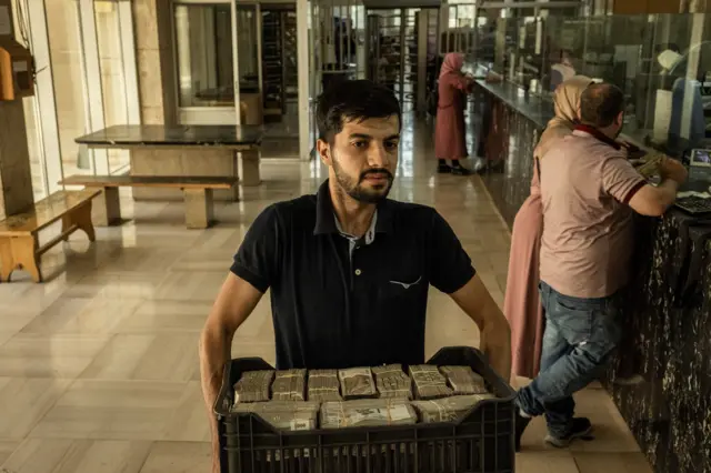 موظف يحمل صندوقاً مليئاً بالأوراق النقدية من فئة 5000 ليرة سوريا في المصرف المركزي السوري في 17 حزيران/حزيران 2025