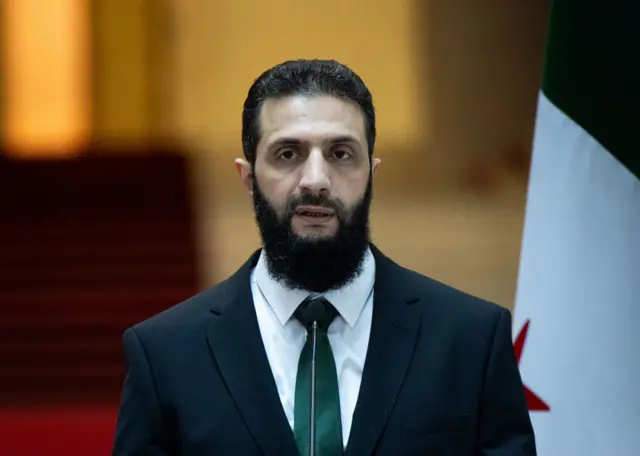 صورة تظهر الرئيس السوري، أحمد الشرع، يرتدي سترة سوداء وربطة عنق خضراء، وقميصاً أبيض.