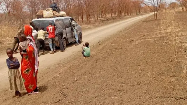 صورة تُظهر رجالاً يدفعون مركبة محملة بالأمتعة على طريق ترابي في السودان.
