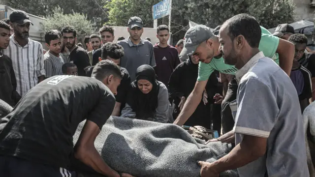 يحمل فلسطينيون جثمان ضحية إلى مستشفى العودة في مخيم النصيرات للاجئين بعد أن أطلقت القوات الإسرائيلية النار على مدنيين ينتظرون المساعدة على طول ممر نتساريم في قطاع غزة في 2 أيلول/أيلول 2025.