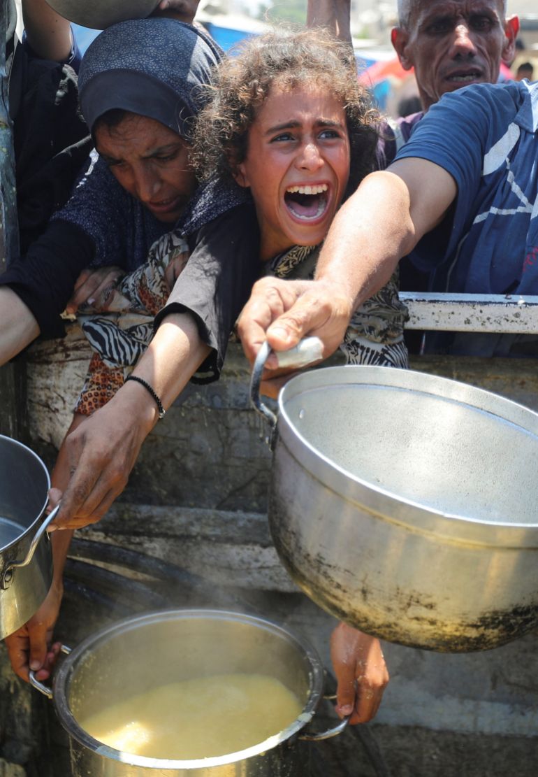 Palestinians react as they wait to receive food from a charity kitchen, amid a hunger crisis, in Gaza City, آب 2, 2025. REUTERS/Mahmoud Issa